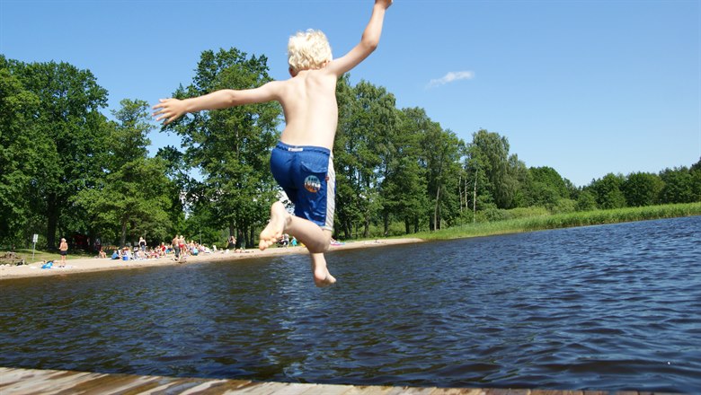Pojke som hoppar i sjön från brygga